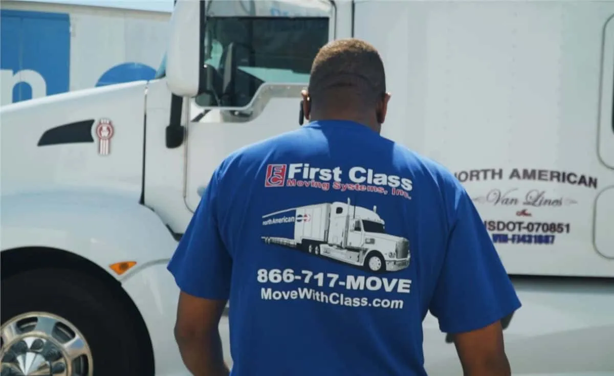 Mover in a First Class Moving Systems shirt standing by a truck
