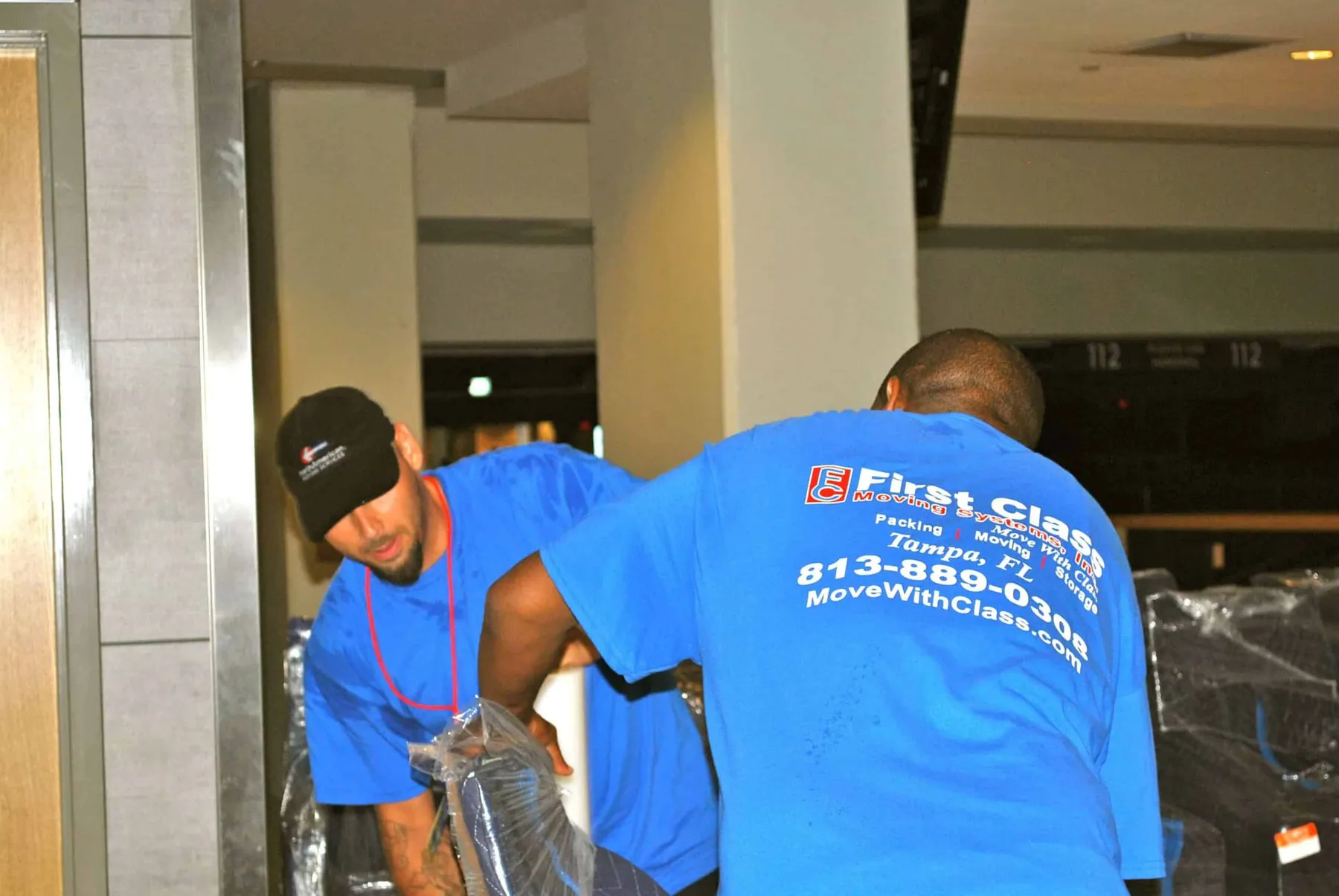 First Class movers wrapping furniture, shirt logo visible