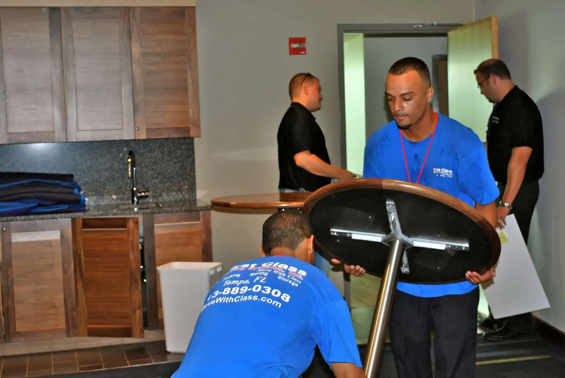 Movers carrying a round table, company shirt visible